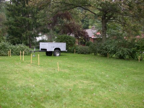 1996 Ford Bronco - A utility trailer sits on a lawn, marked by wooden stakes, with a house and trees in the background.