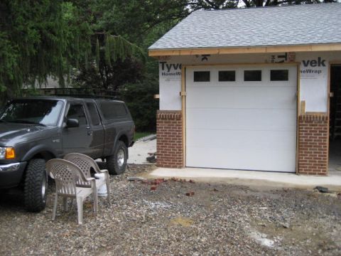 1996 Ford Bronco - A gray pickup truck with a camper shell is parked next to a garage that is under construction, with a new garage door installed.