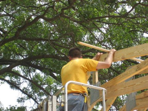 1996 Ford Bronco - Construction worker on a lift assembling wooden beams under a large tree.