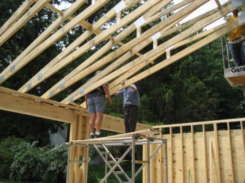 1996 Ford Bronco - Workers are seen installing roof trusses on a building under construction, with trees and a suburban house visible in the background.