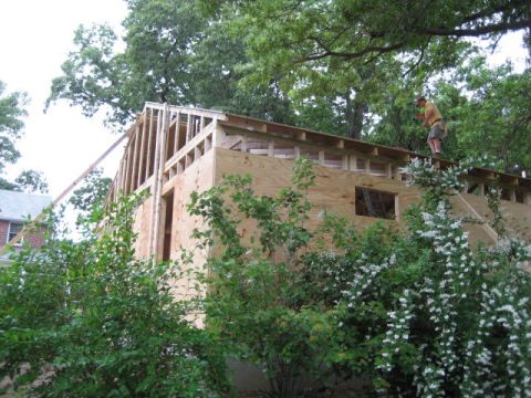 1996 Ford Bronco - A person stands on the roof of a wooden structure under construction, with trees and bushes in the foreground.