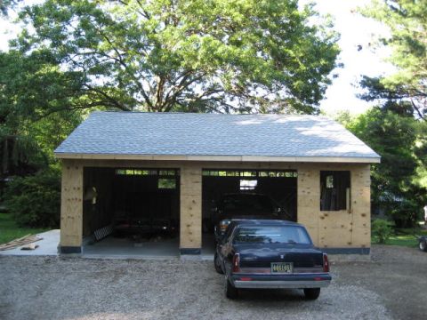 1996 Ford Bronco - A dark sedan is parked in front of a two-bay garage that is still under construction.