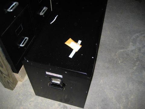 1996 Ford Bronco - A black filing cabinet sits on a concrete floor, with some debris on its surface.