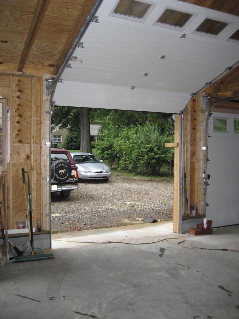 1996 Ford Bronco - View from inside a garage shows two cars parked outside on a gravel driveway.