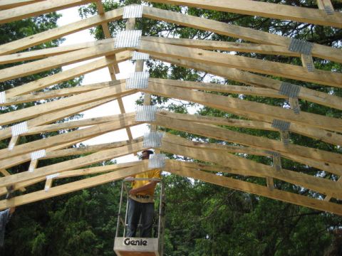 1996 Ford Bronco - Construction worker on a lift amidst wooden roof trusses, with trees visible.