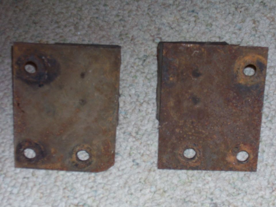 two rusty metal brackets with four holes each