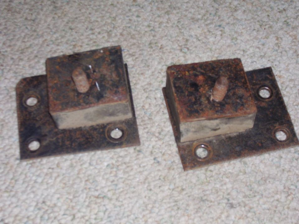 Two rusty metal brackets with rubber blocks and bolts, resting on carpet