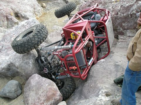 1986 Toyota Hilux - A custom-built off-road buggy is stuck on its side amidst large rocks on a trail.