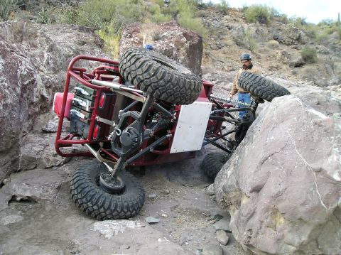 1986 Toyota Hilux - An off-road buggy is stuck and tilted on a rocky terrain, with a person observing the situation.