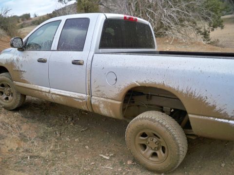 2005 Dodge 1500 - A muddy silver pickup truck drives off-road.
