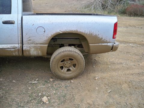 2005 Dodge 1500 - This silver pickup truck, likely a 2005 Dodge 1500, is seen from the rear side, heavily coated in mud from off-road use.