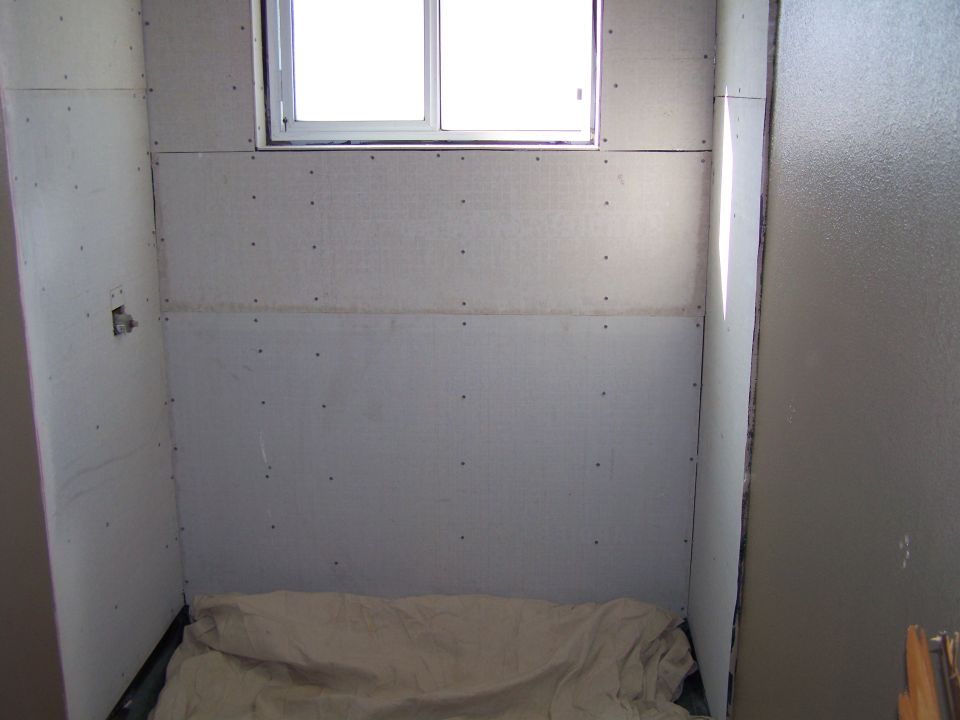 Interior of a room with unfinished drywall and a window. A sheet covers the floor