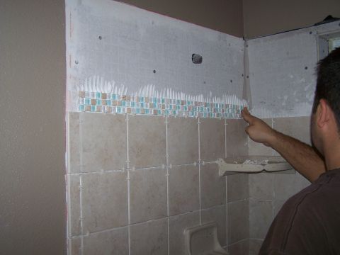 1991 Ford Bronco - A person is installing tiles on a shower wall, with a decorative mosaic border being applied.