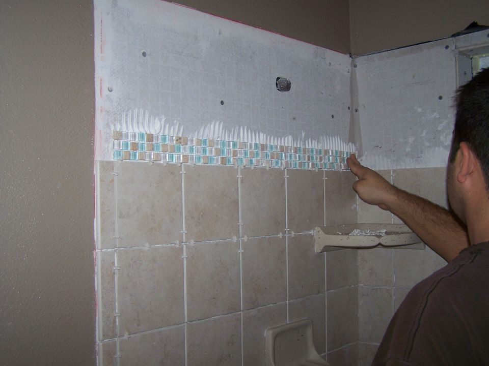Man tiling a shower wall with beige and blue mosaic tiles