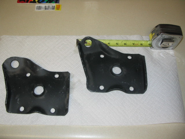 Pair of black stamped steel mounting brackets on a counter with a tape measure