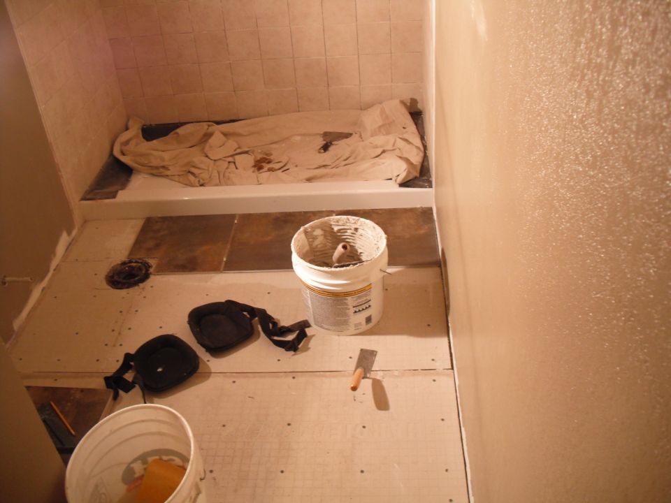 Bathroom renovation in progress with bathtub, tile, buckets, and tools on the floor