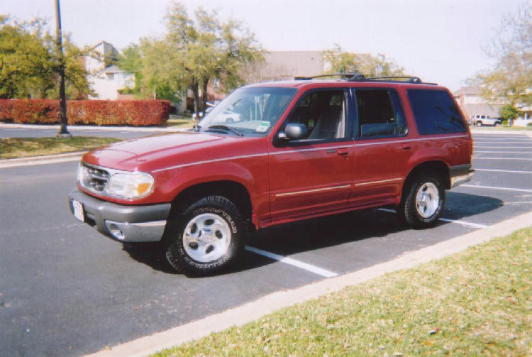 Red Ford Explorer SUV with tan cladding parked in a parking lot, front three-quarter view