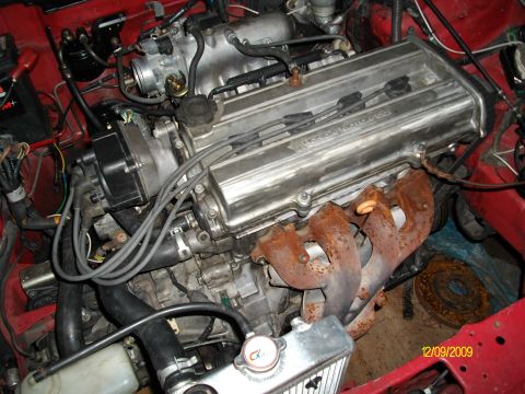 1989 Ford Bronco - Close-up view of a Honda engine in a red vehicle, showing the exhaust manifold and various hoses.