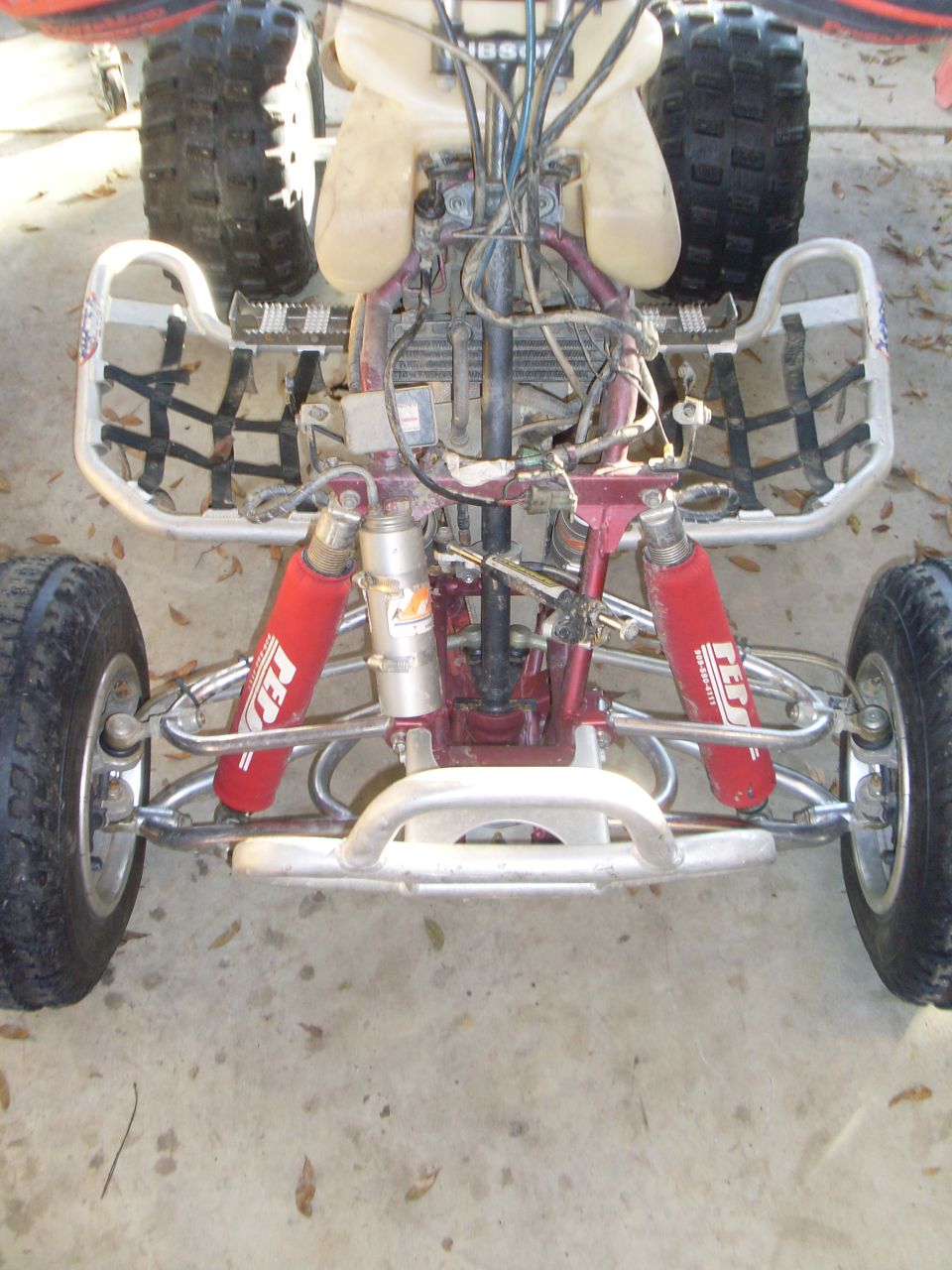 Front view of an ATV's suspension and engine area. Red shocks are visible