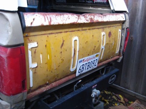 1989 Ford Bronco - The tailgate of a yellow Ford truck displays the brand name in white lettering, accompanied by a California license plate.
