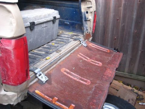 1989 Ford Bronco - The rusty tailgate of a pickup truck is open, revealing a toolbox in the bed.