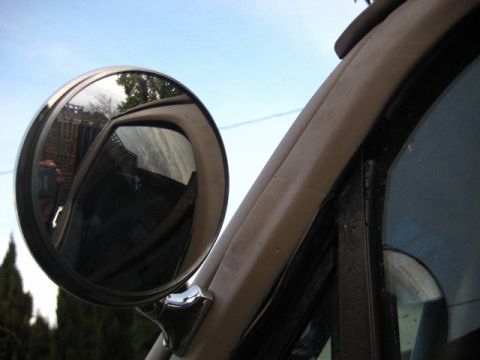 1989 Ford Bronco - Close-up of a vehicle's side mirror and door frame, with a reflection of the surroundings.