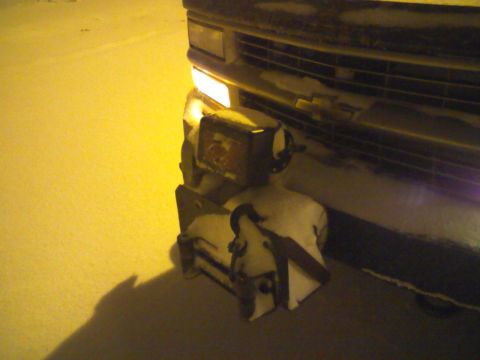 2000 Chevrolet Tahoe - A vehicle's front bumper is obscured by snow, with a snow plow attachment mounted and a headlight illuminated.