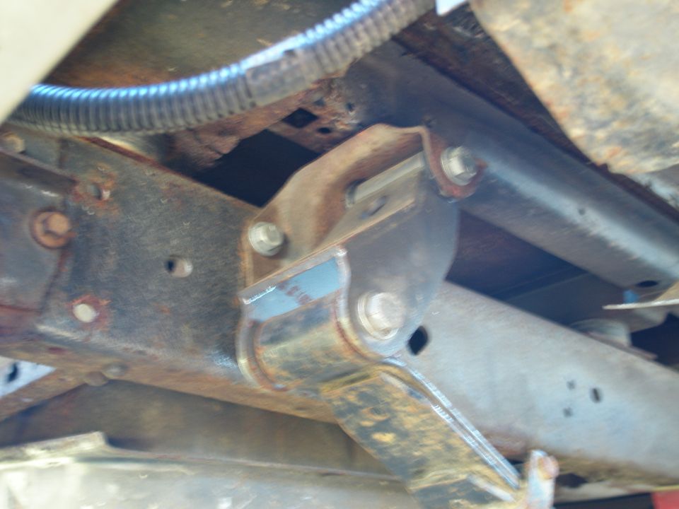 Underbody shot of rusty frame rail and bolted bracket mount with flexible metal conduit above
