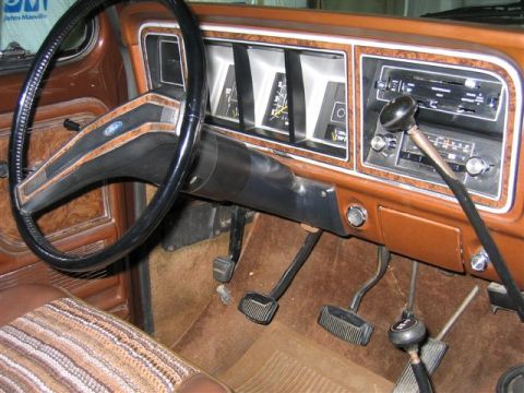 1978 Ford Bronco - The interior of a 1978 Ford Bronco features woodgrain trim on the dashboard and door panels, a large steering wheel, and a floor-mounted sh…