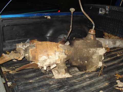1991 Ford Bronco - A heavily rusted drivetrain component, possibly a transfer case, rests in the bed of a pickup truck.