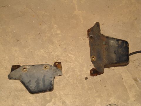 1991 Ford Bronco - Two metal brackets, one black and one rusty, lie on a concrete surface.