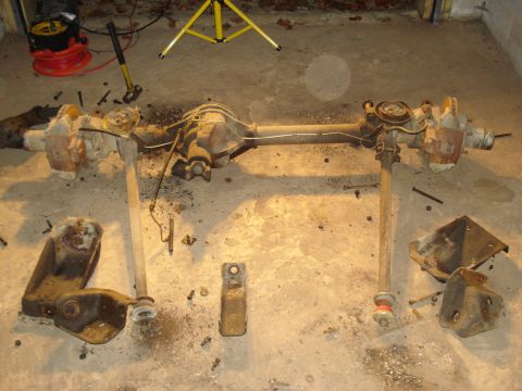 1991 Ford Bronco - Disassembled front and rear axles lie on a concrete surface, surrounded by tools and debris.