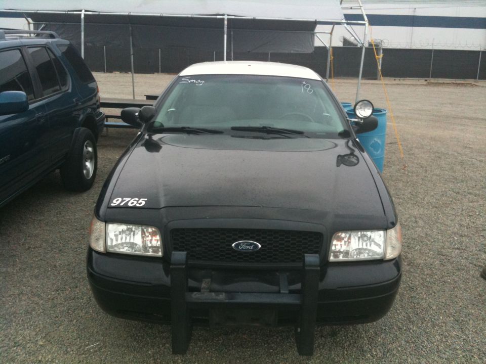 Front view of black Ford sedan with push bumper in a dirt lot
