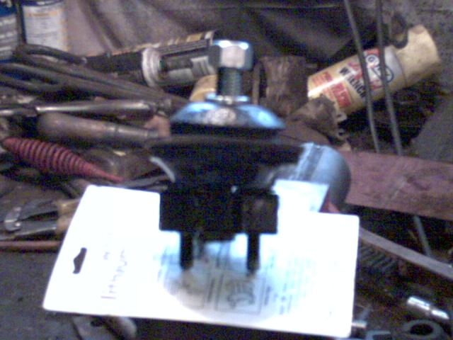 Blurry black automotive component on a card amid tools in a cluttered shop