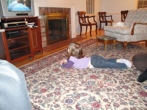 2000 Ford Crown Victoria - A young child lies on a patterned rug, engrossed in a television program in a cozy living room.
