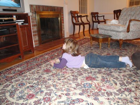 2000 Ford Crown Victoria - A young child lies on a carpeted floor, engrossed in watching a television set in a living room.