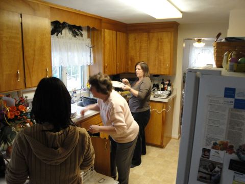 2000 Ford Crown Victoria - Three women are busy in a kitchen, with one at the sink and another holding plates.