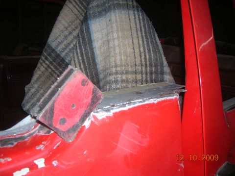 1985 Ford Bronco - A red vehicle's interior is undergoing repairs, with a plaid seat cover visible and metal edges being worked on.