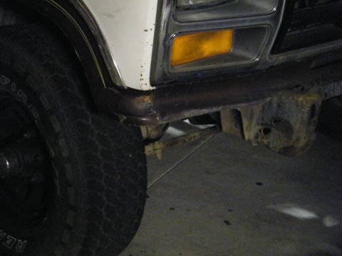 1982 Ford Bronco - Close-up of the front corner of a vehicle, highlighting the tire, bumper, and headlight area.
