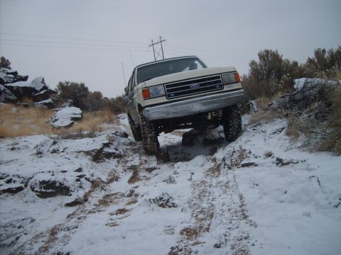 1989 Ford Bronco - A white Ford Bronco navigates a challenging snowy terrain with rocky obstacles.