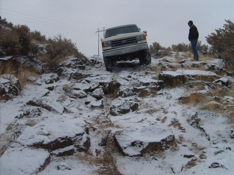 1989 Ford Bronco - A 1989 Ford Bronco tackles a challenging, snow-dusted rocky terrain, with a person observing from the side.