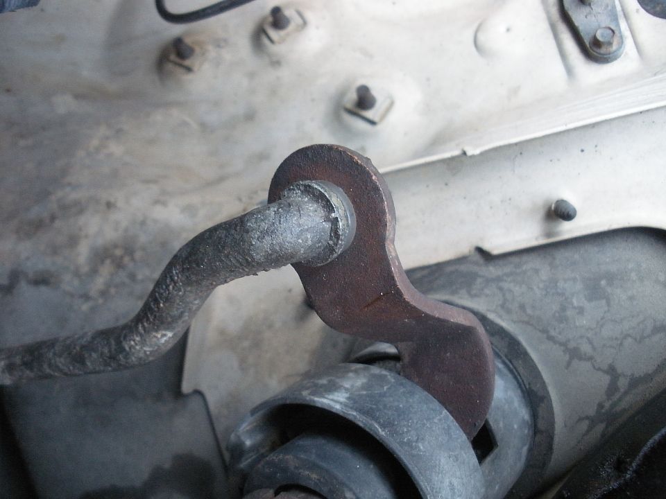 Close-up of rusty metal linkage connected to a black rubber bushing, likely part of a steering column