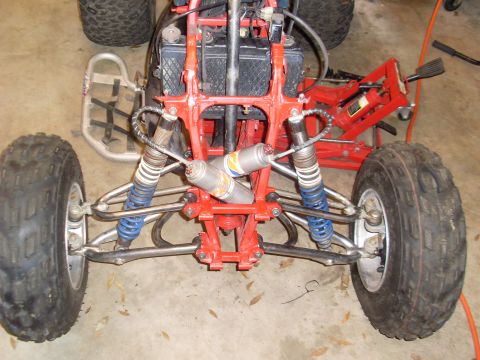 1987 Honda 250 R - Close-up view of the front suspension system of an ATV, showing the red frame and dual shock absorbers.