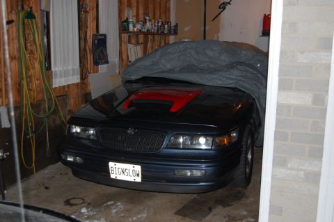 1985 Mercury Grand Marquis - A dark blue sedan with a red hood scoop is parked in a garage, partially covered by a grey tarp.