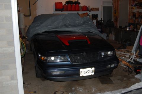1985 Mercury Grand Marquis - A dark blue sedan with a red hood scoop is partially covered in a garage.
