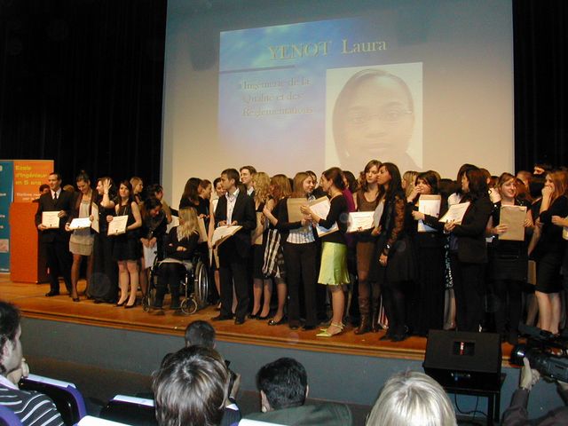 Graduation ceremony with students on stage receiving awards, a screen displays text and a photo