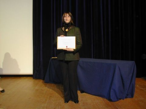 1991 Ford Crown Victoria - A woman stands on a stage holding a certificate, with draped curtains behind her.