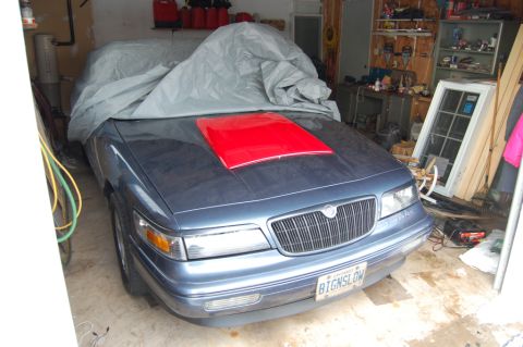 1985 Mercury Grand Marquis - A Mercury Grand Marquis with a red hood scoop is parked in a garage, mostly covered by a tarp.