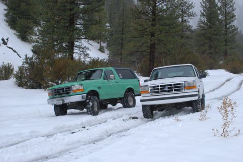 1996 Ford Bronco - Two Ford Broncos driving on a snowy mountain road.