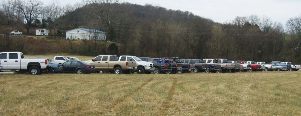 Side view of multiple pickup trucks and cars parked in a grassy field